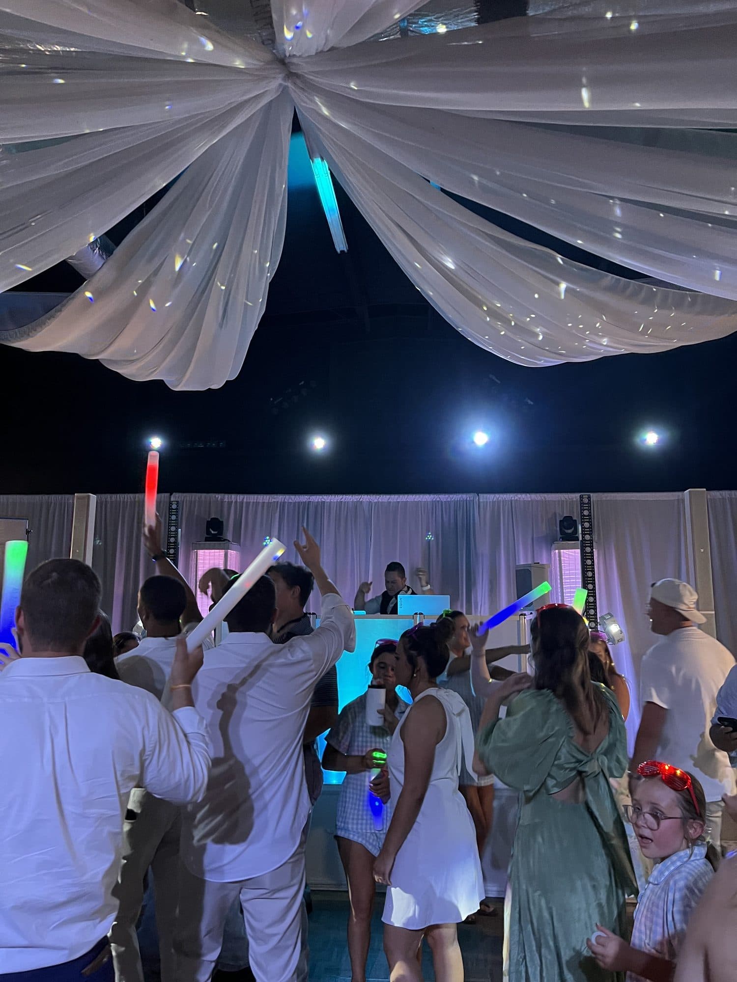 Guests waving light-up foam batons on the dance floor beneath draped ceiling fabric
